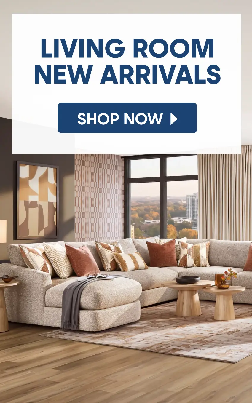 LIVING ROOM NEW ARRIVALS SHOP NOW. A modern living room featuring a beige sectional sofa with patterned pillows and wood tables.