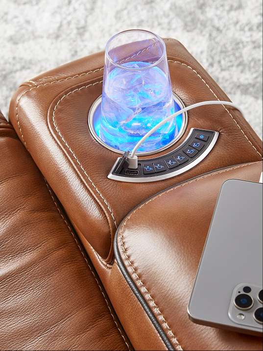 Brown leather recliner with a built-in cup holder, USB ports, and control panel. A glass of water with ice is in the cup holder. A phone is charging.
