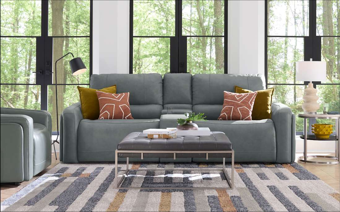 A gray leather sofa with decorative pillows, an ottoman, and a patterned rug.
