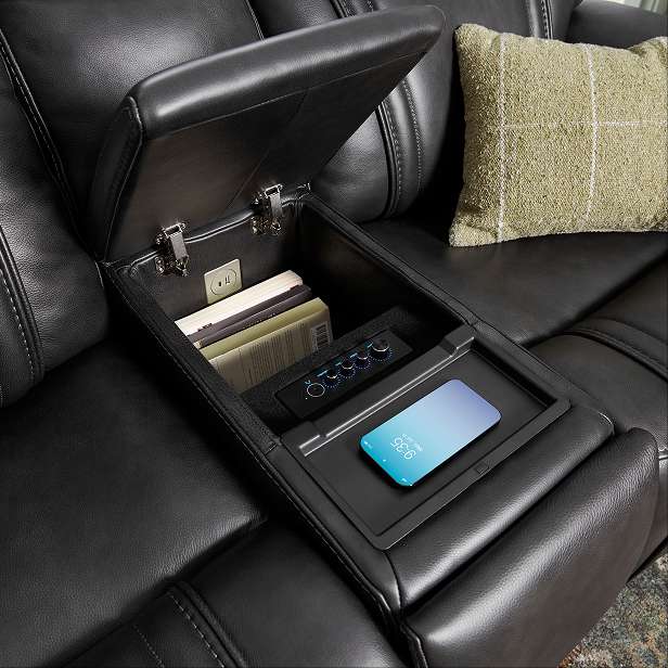 Black leather sofa with an open storage compartment, a phone, and books.
