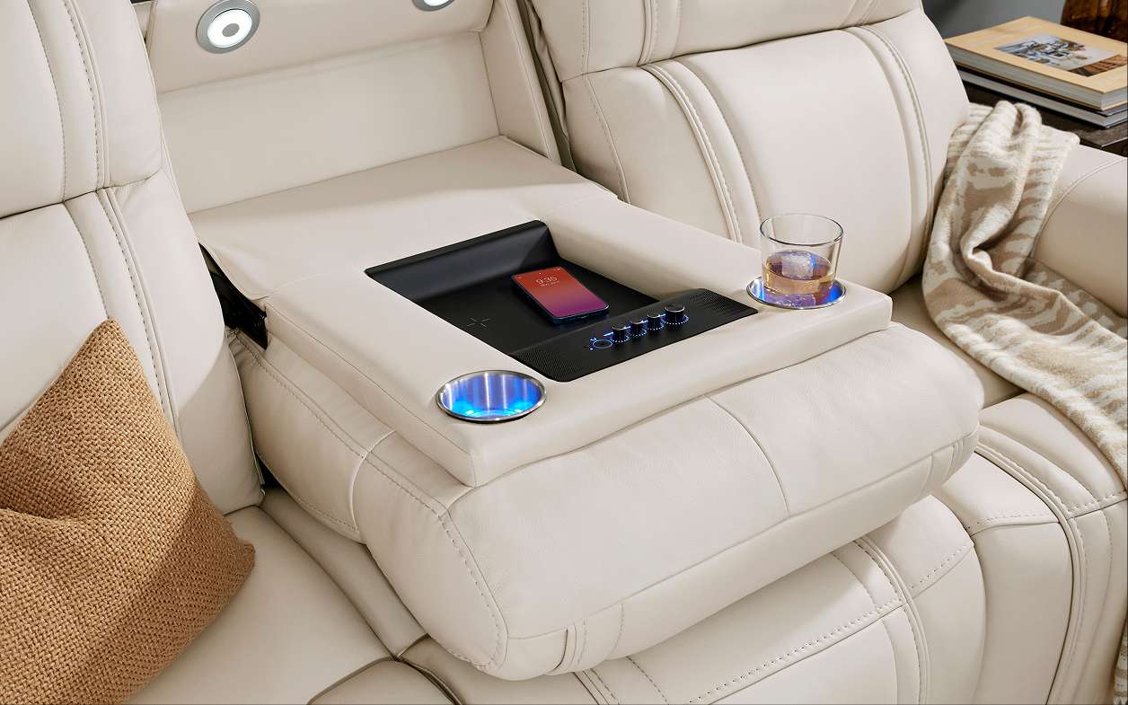 Cream-colored leather recliner with a built-in console featuring a phone charger, cup holders, and controls.
