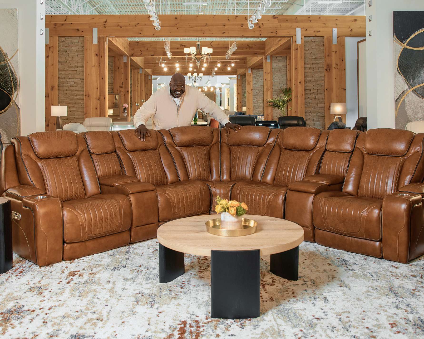 A large brown leather sectional sofa with a round coffee table and a man standing behind it.
