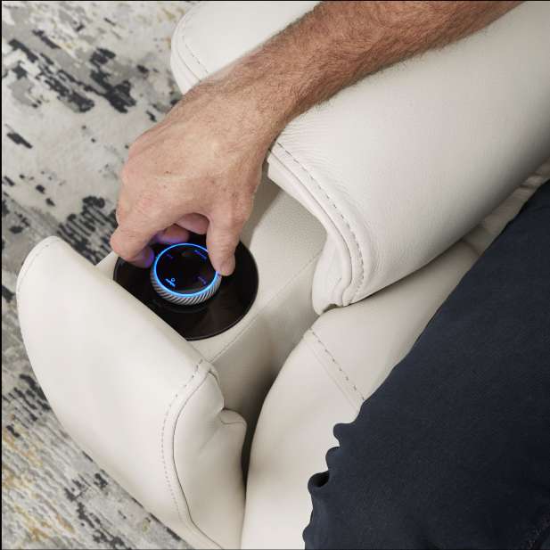 A person's hand adjusting a control panel on a cream-colored recliner.
