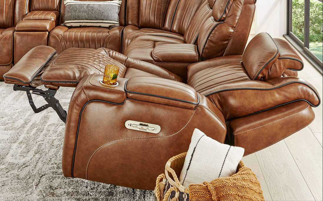 Brown leather reclining sectional sofa with cup holders and a basket with pillows.
