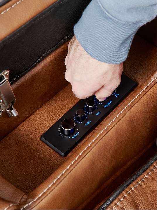 A hand adjusting the controls on a black panel with volume, treble, bass, and vibration settings.
