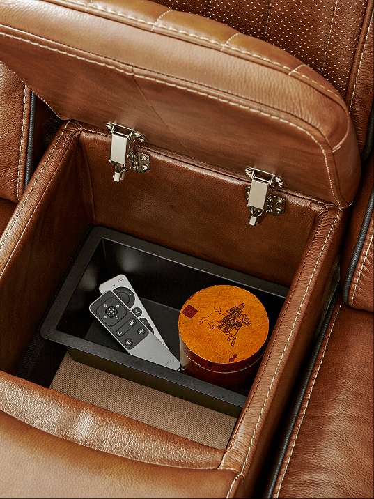 Brown leather sofa with a storage compartment containing a remote and a round container.
