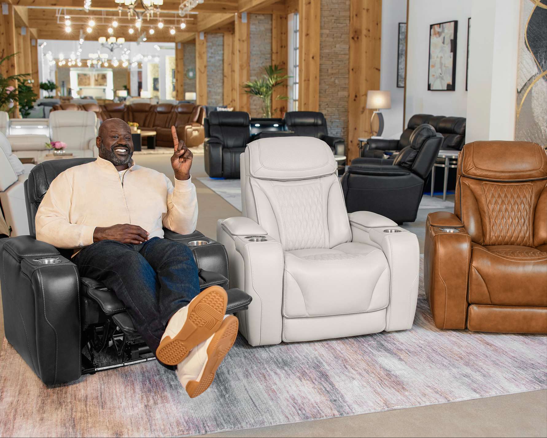 Shaquille O'Neal sitting in a black recliner, pointing up. Other recliners are in the background.
