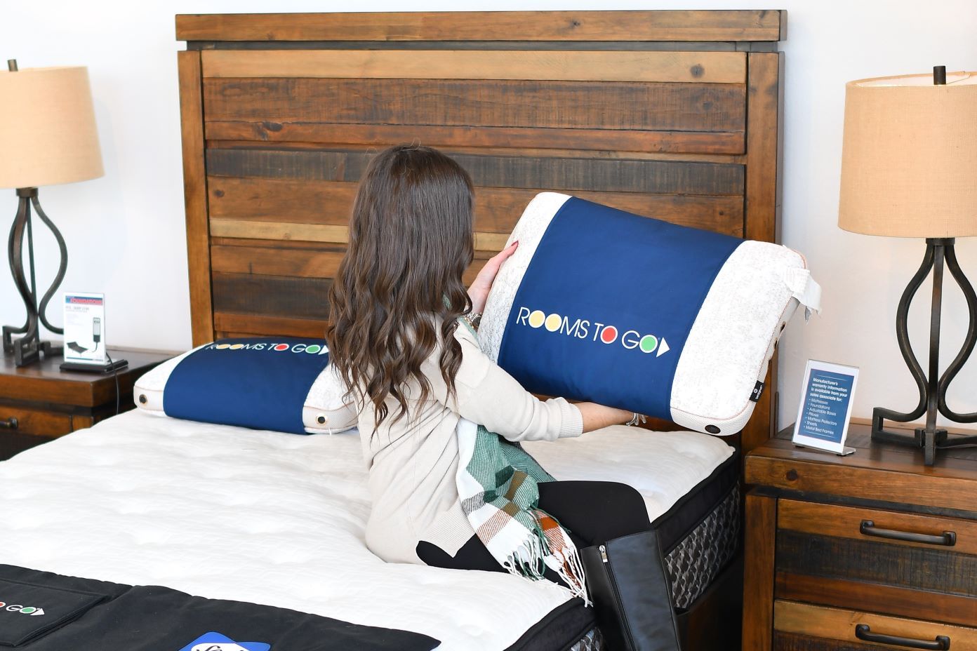 Rooms To Go pillow. A woman is holding a pillow on a bed.

