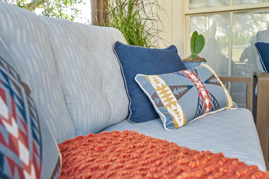 A light blue outdoor sofa with patterned pillows and an orange throw.
