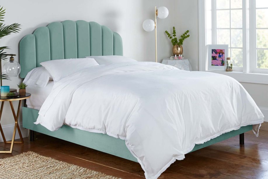 A bed with a teal headboard and white bedding.
