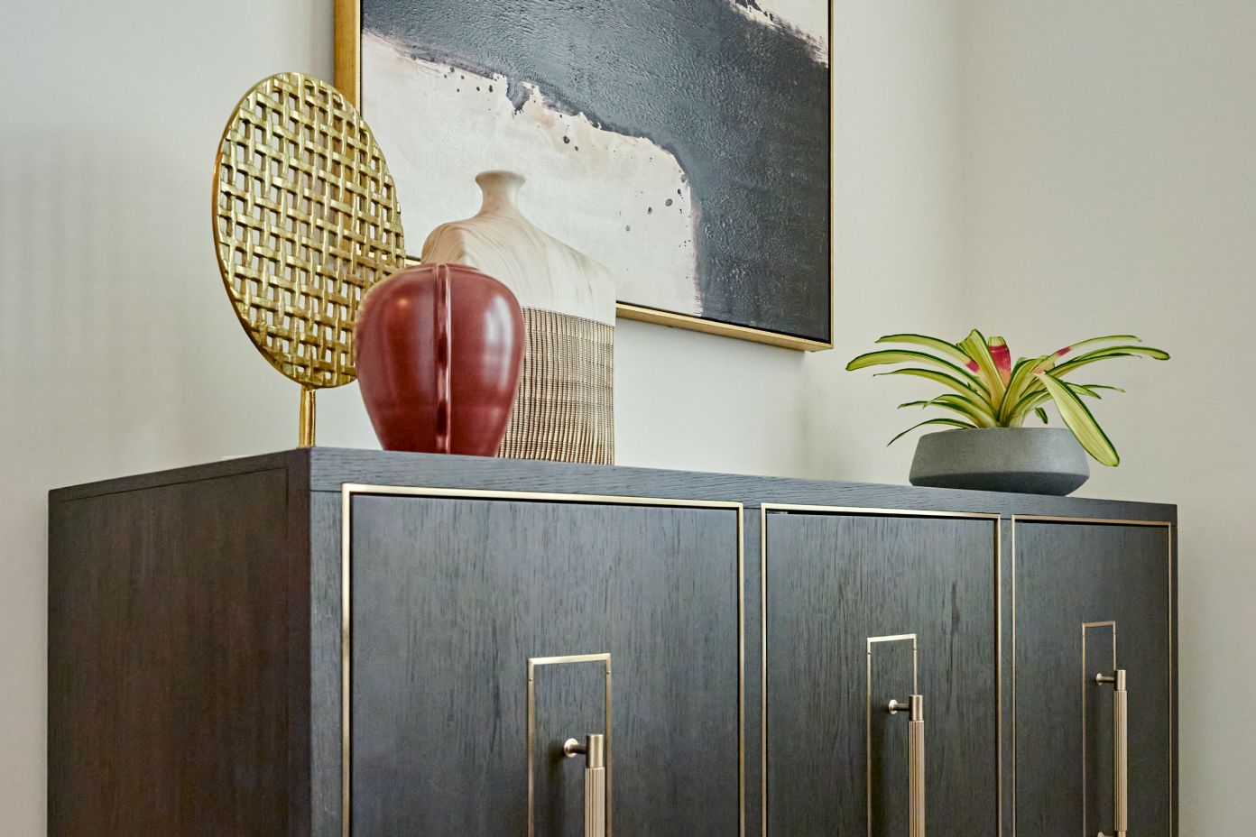 Dark wood cabinet with gold trim, topped with decorative objects and a potted plant.
