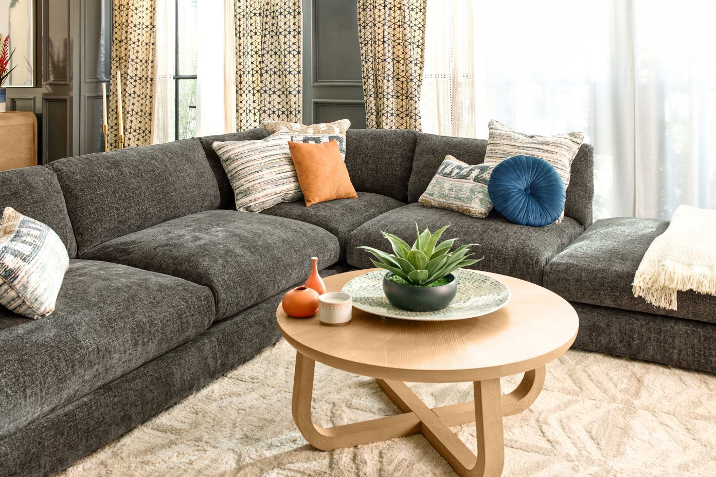 A gray sectional sofa with decorative pillows and a round wooden coffee table.
