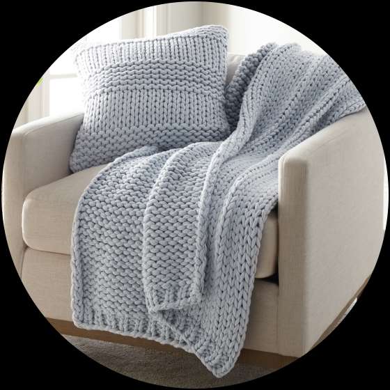 A light blue knitted throw blanket and pillow on a beige armchair.
