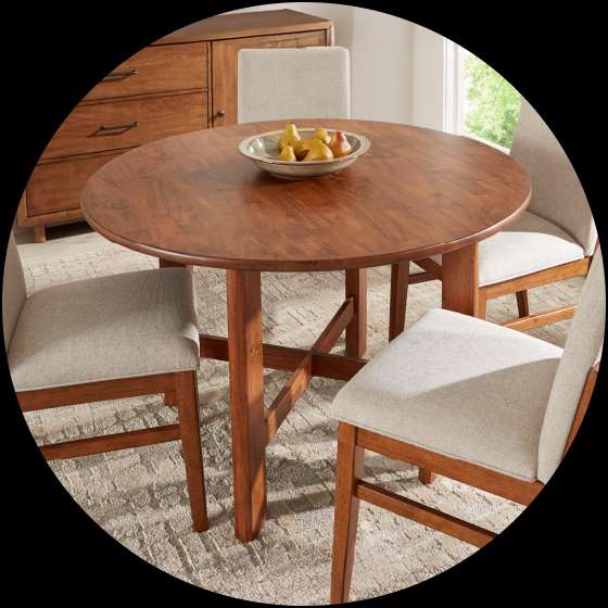 A round wooden dining table with four chairs and a buffet.

