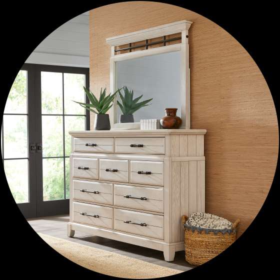 White dresser with a mirror, plants, and a basket.
