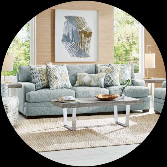 Living room with a blue sofa, patterned pillows, a wooden coffee table, and a beige rug.
