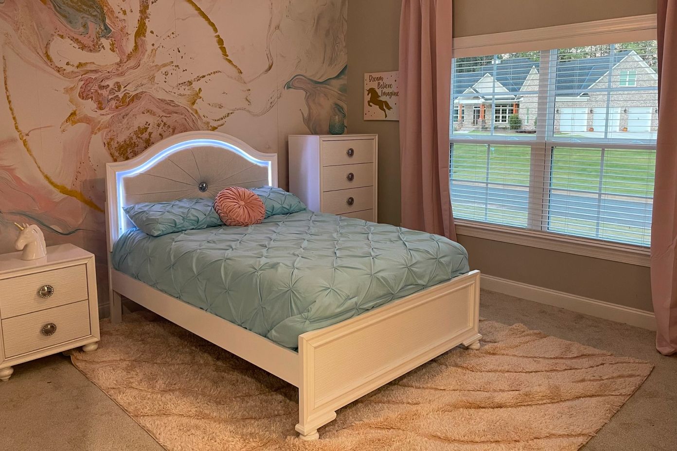 A bedroom with a white bed, a rug, and a window with blinds.
