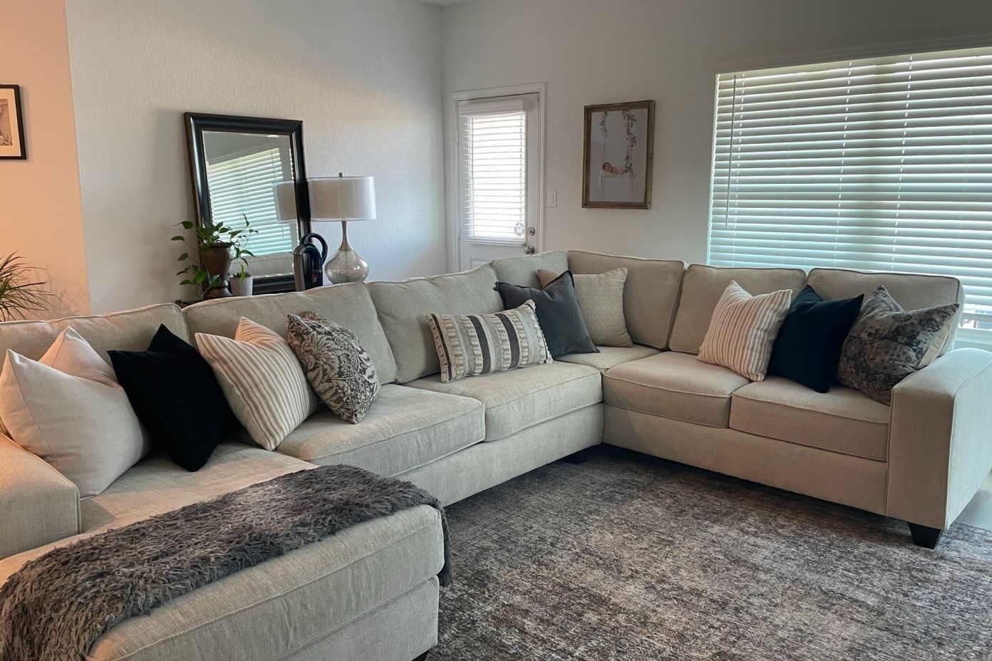A beige sectional sofa with decorative pillows and a gray rug.
