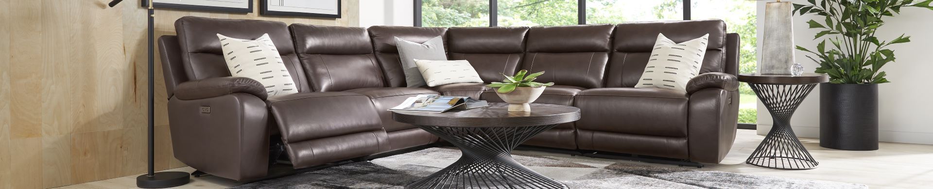 Brown leather sectional sofa with pillows and a round coffee table.
