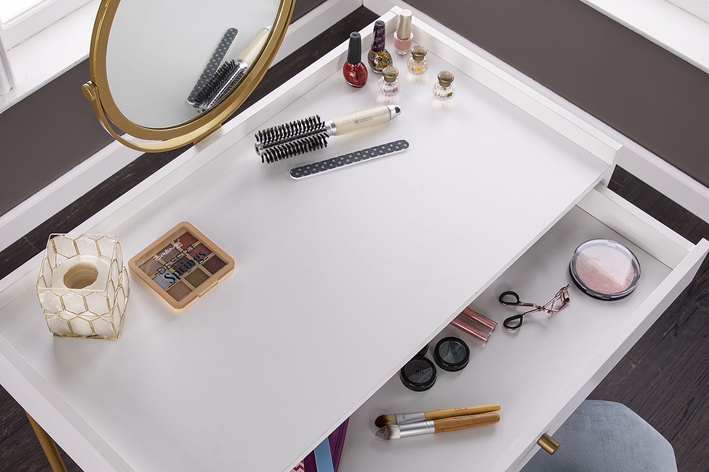 White vanity table with a mirror, makeup, and a drawer.
