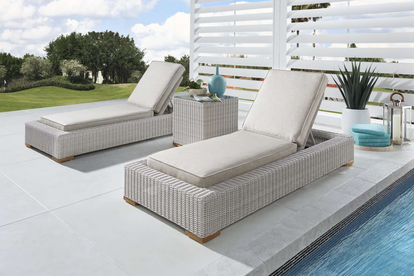 Two gray wicker chaise lounges with beige cushions next to a pool.

