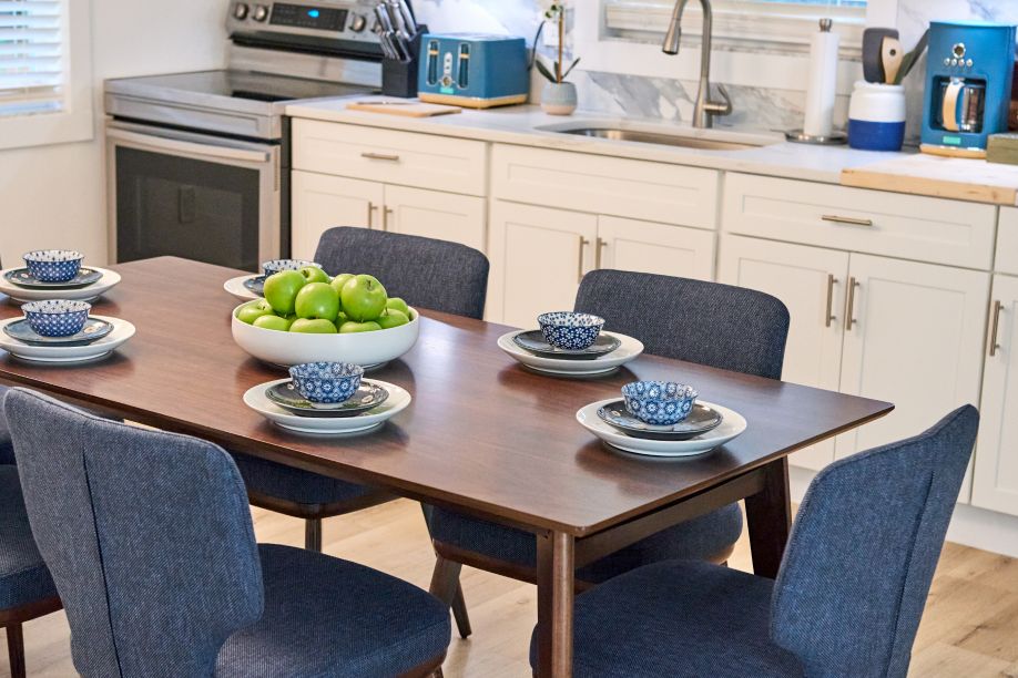 A dining table set with six blue chairs and a bowl of green apples.
