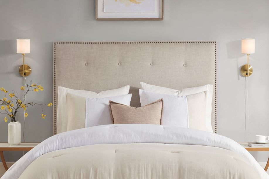 Bedroom with a beige headboard, white bedding, and gold sconces.
