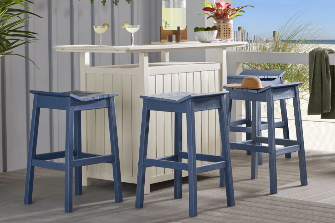 Blue bar stools with a white bar in a beach setting.
