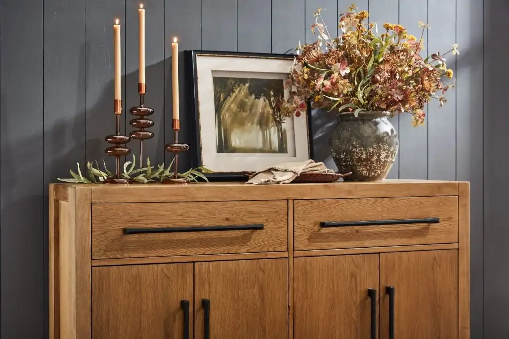 Wooden cabinet with candles, artwork, and a vase of flowers.
