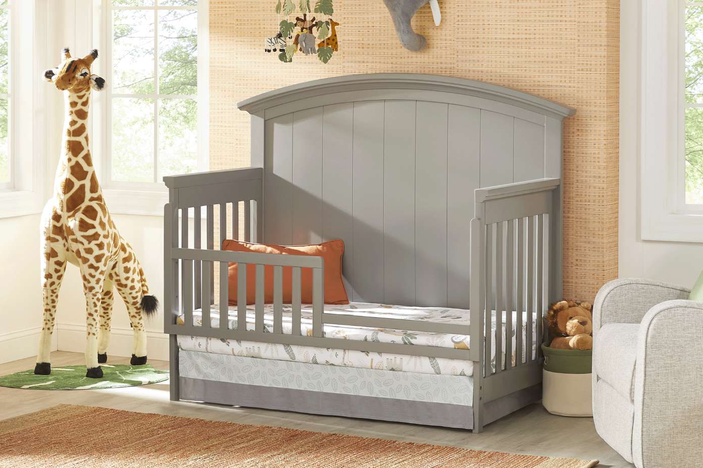Gray crib with a giraffe and a rug in a nursery.
