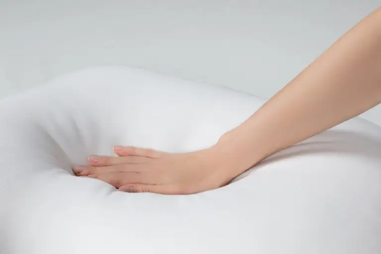 A hand pressing into a soft, white memory foam pillow, demonstrating its plush texture and responsiveness.