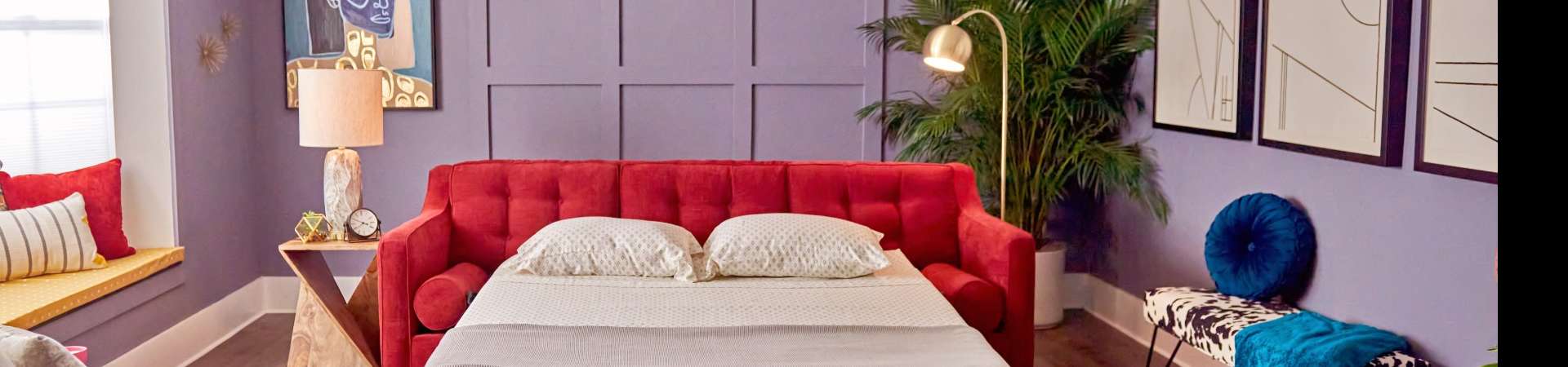 Red sofa bed with pillows and a side table with a lamp.
