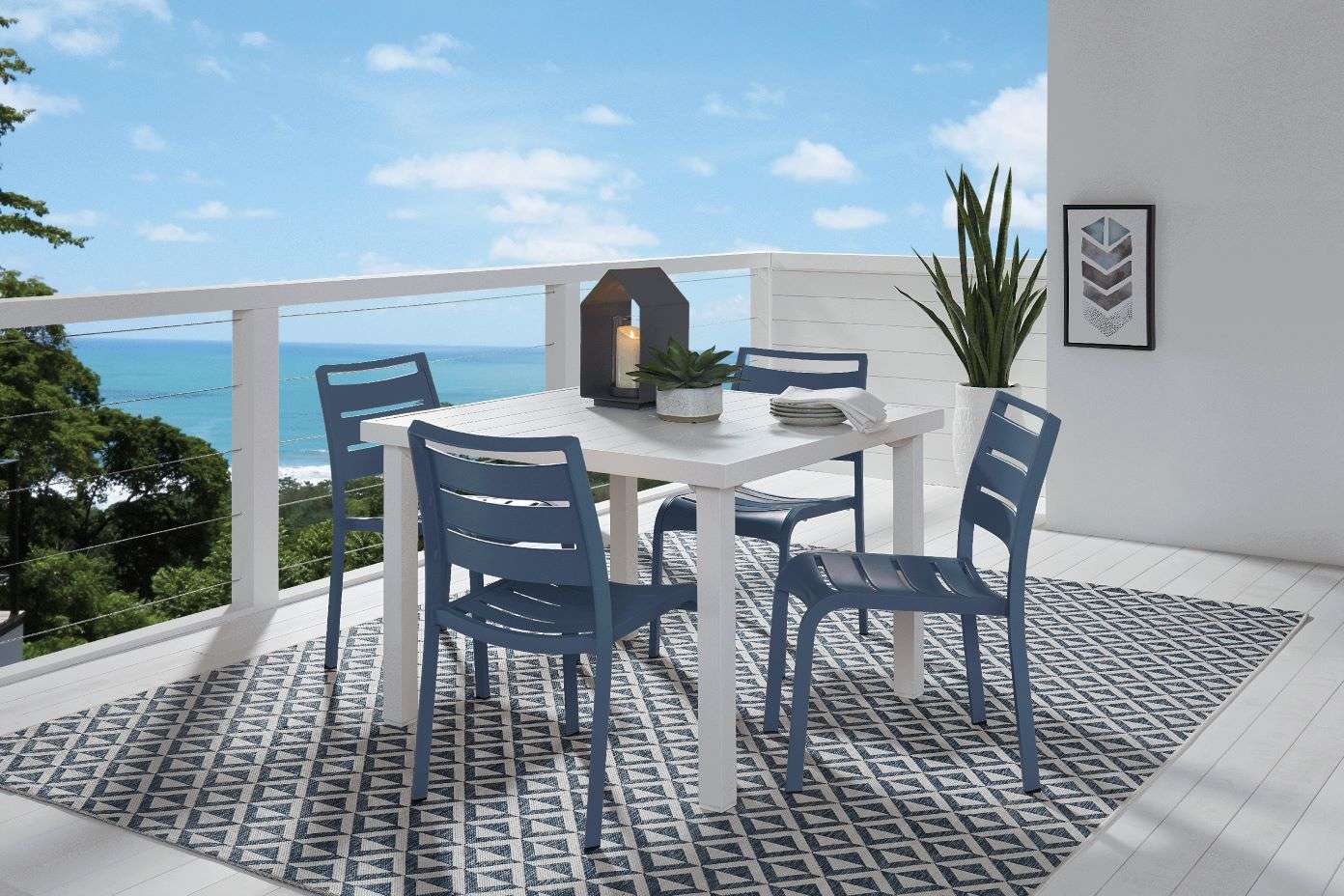Outdoor dining set with a table, chairs, and rug on a deck overlooking the ocean.
