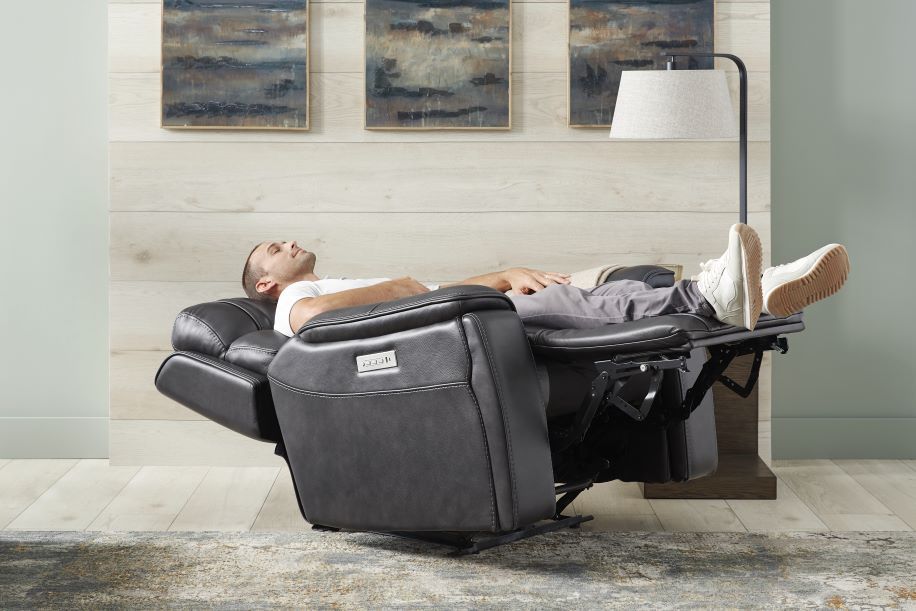 A man is relaxing in a black recliner chair with his feet up.

