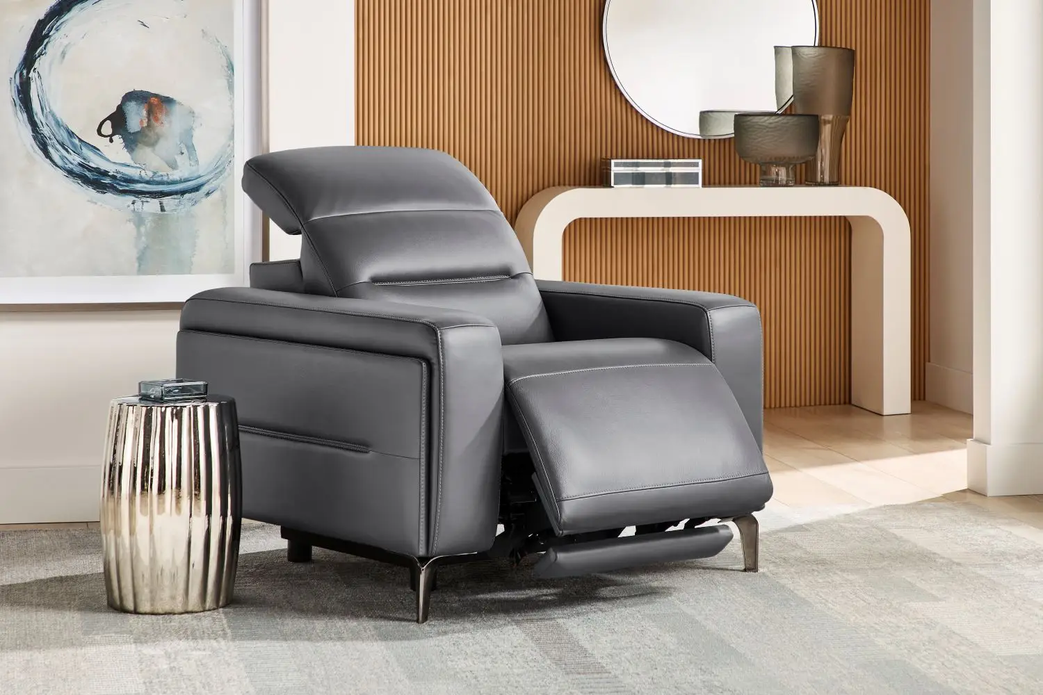 A modern gray leather recliner chair with a metal base, positioned next to a metallic side table in a contemporary room.