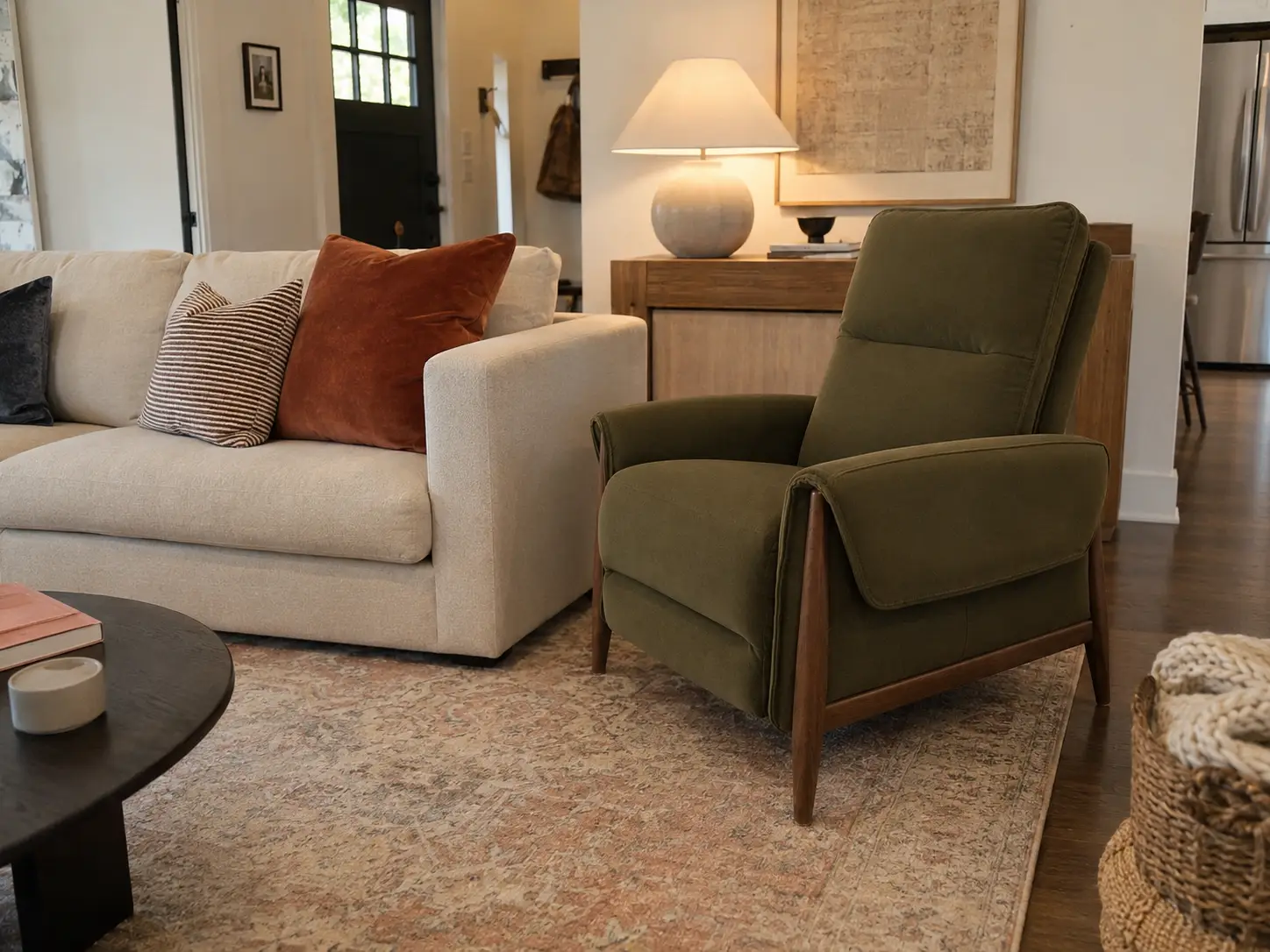An olive green mid-century modern armchair sits on a patterned rug next to a cream-colored sofa with decorative pillows.