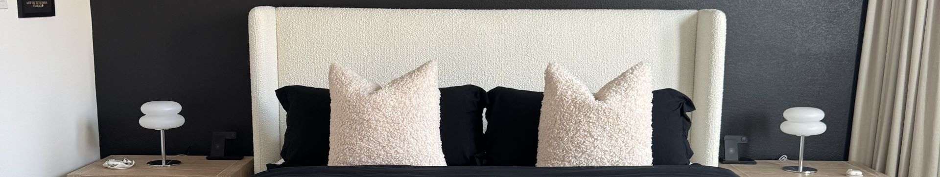Bedroom with a white headboard, black pillows, and bedside lamps.
