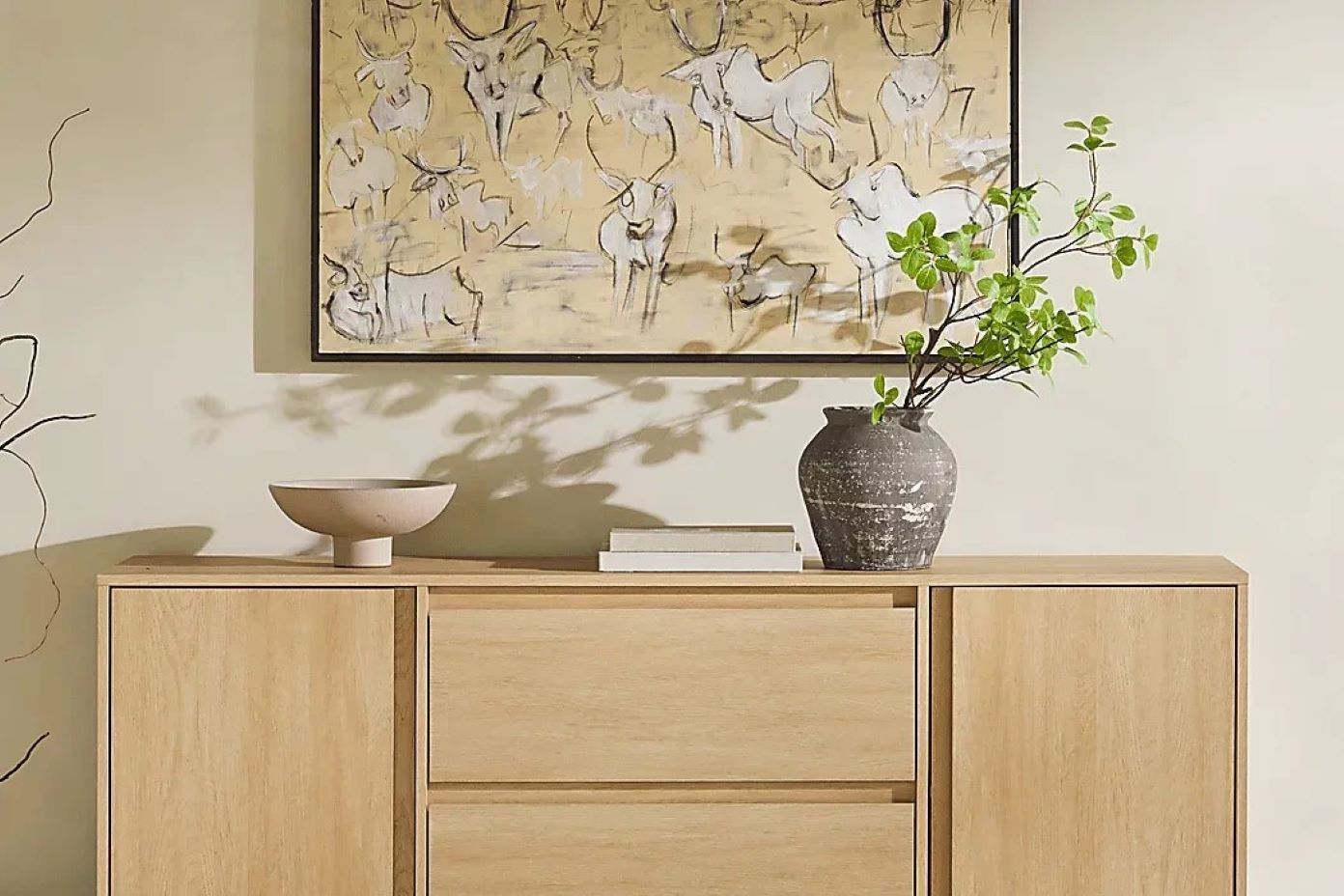 Wooden cabinet with a painting, a vase with greenery, a bowl, and books.
