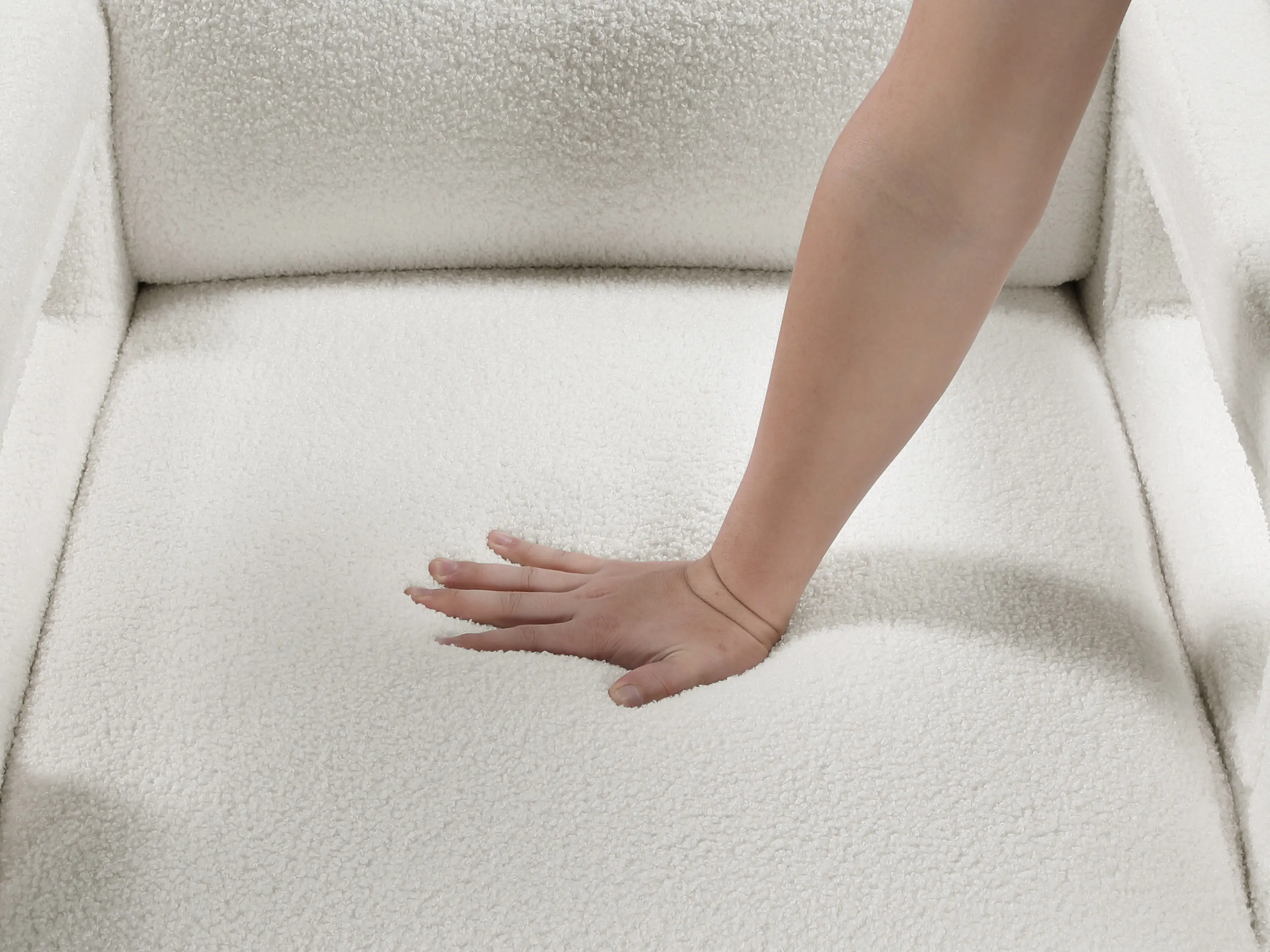 A hand pressing down on the soft, white, textured fabric of a modern armchair seat.