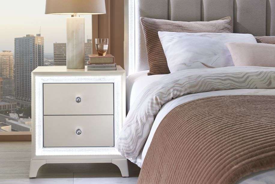 Nightstand with LED lights and crystal knobs next to a bed with pillows and a blanket.