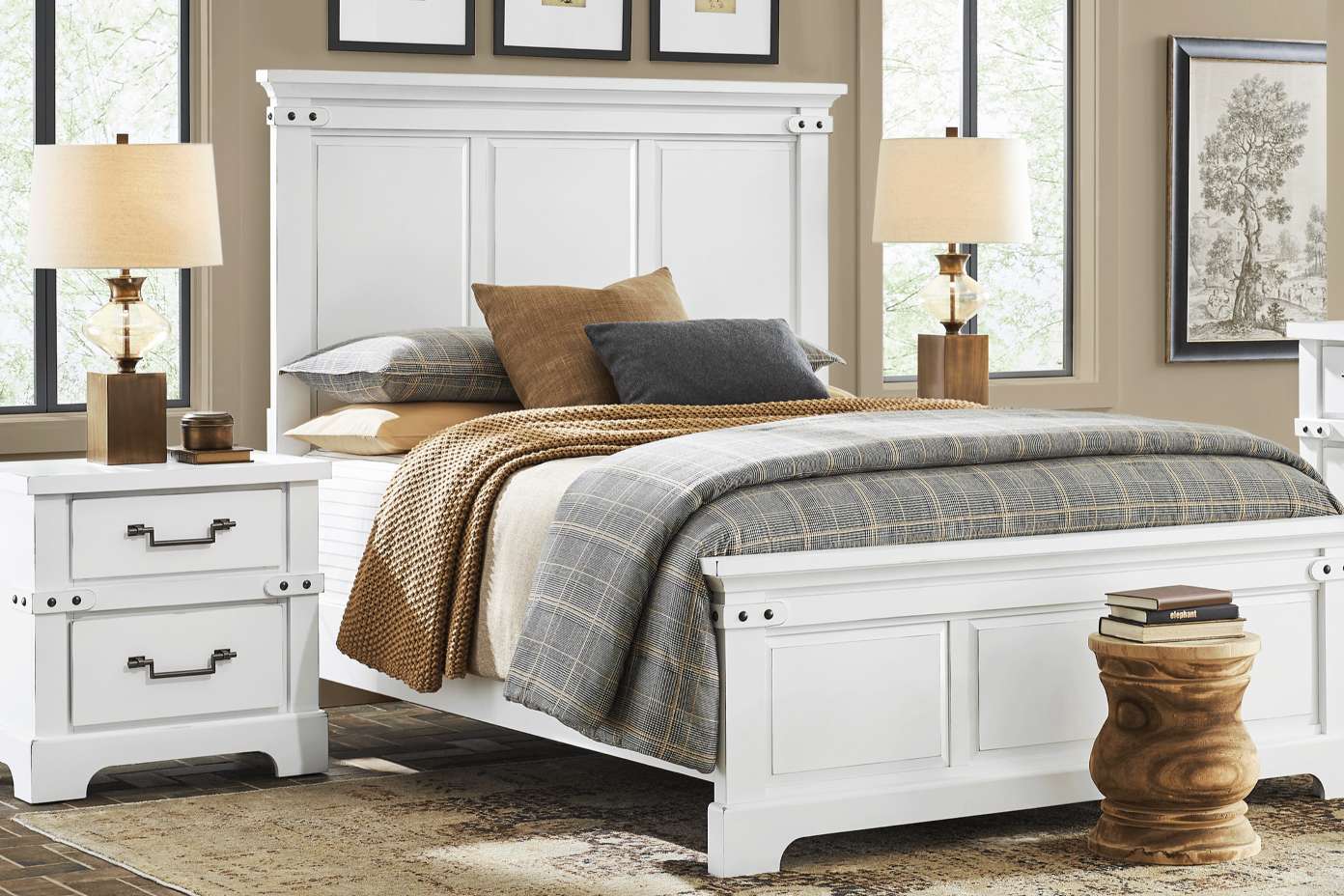 White bed with a plaid blanket and pillows, two nightstands with lamps, and a wooden stool.