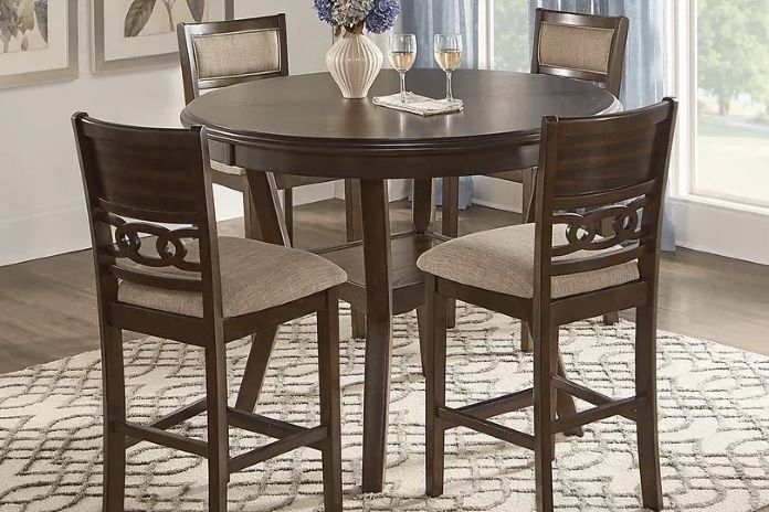 A dark brown round dining table with four matching bar stools on a patterned rug.
