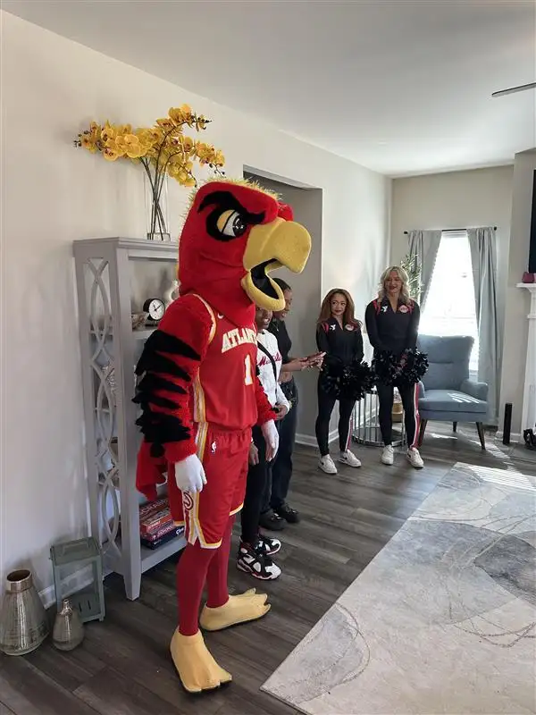 The Atlanta Hawks mascot, cheerleaders, and a group of people are in a living room.
