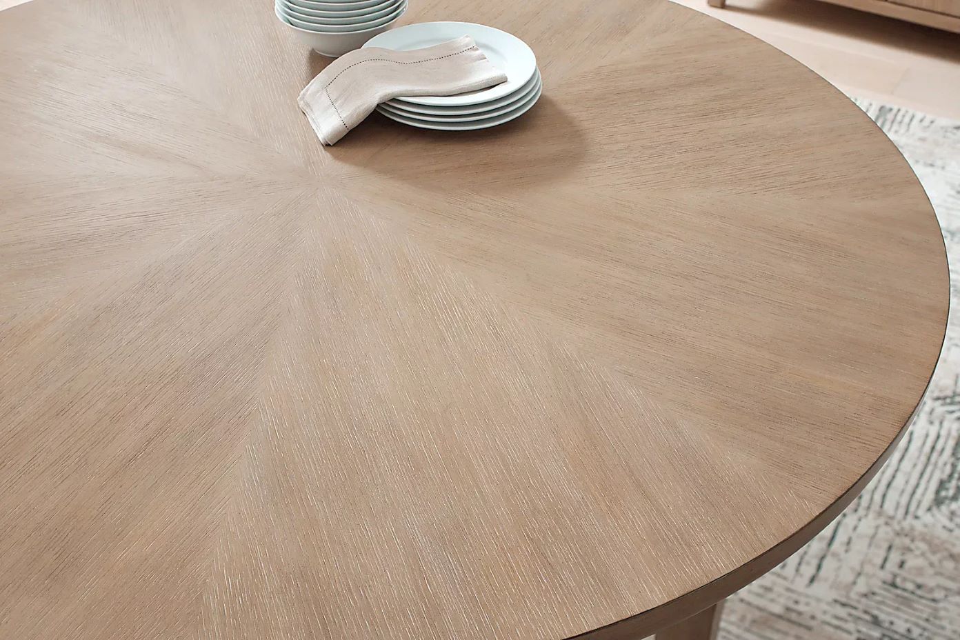 A round wooden dining table with plates and a napkin.
