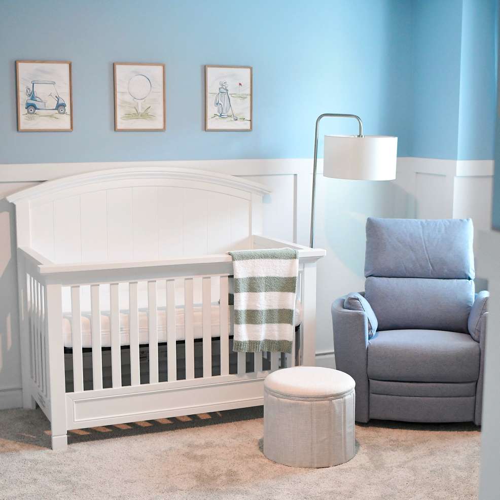 A nursery with a white crib, blue recliner, and golf-themed artwork.
