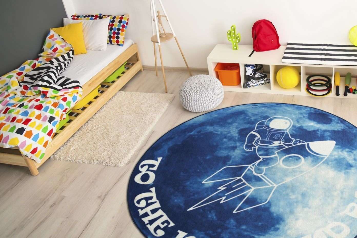 A child's bedroom with a bed, rug with an astronaut, and storage unit.