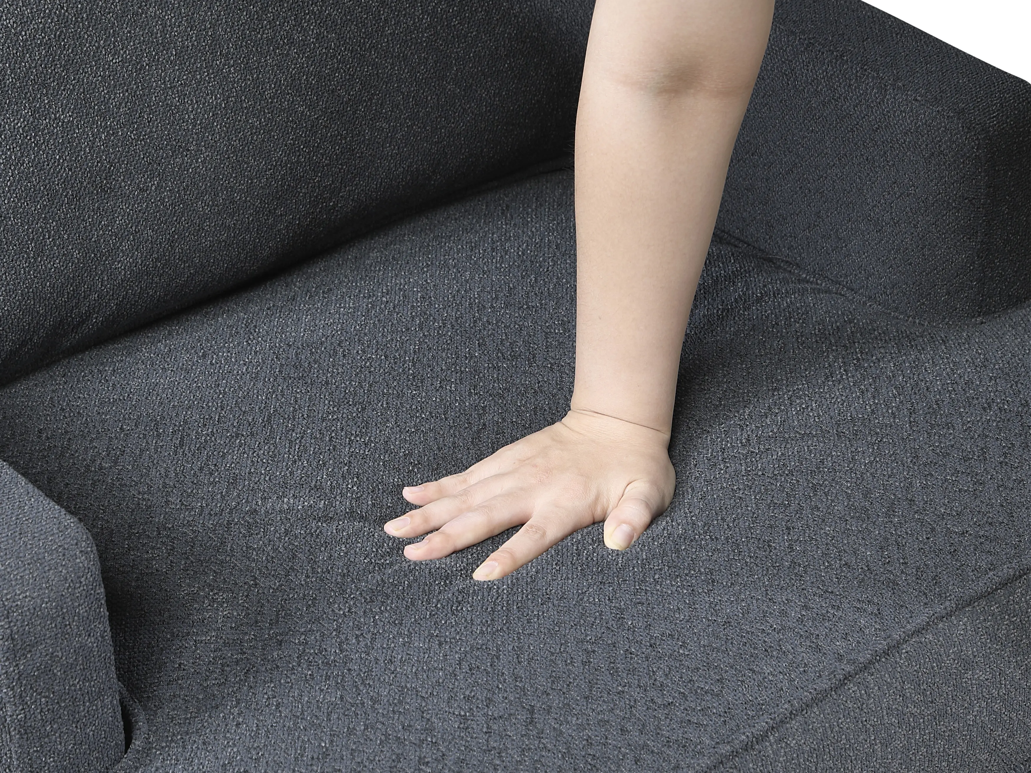 A person's hand pressing down on the textured, dark gray fabric of an upholstered chair.