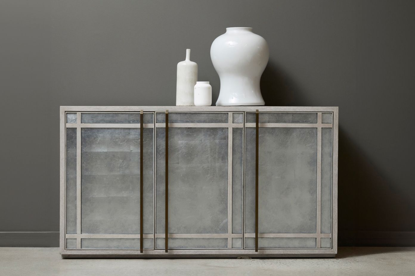 A gray cabinet with three white vases on top.
