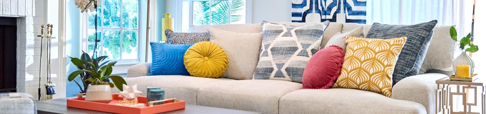 A beige sofa with several colorful pillows. A tray with decor sits on a coffee table.
