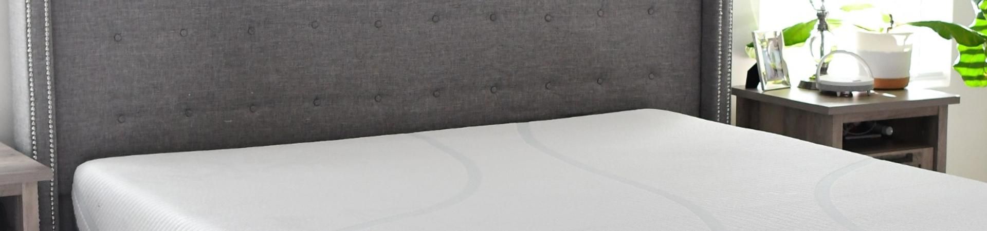 A bed with a gray headboard and a white mattress.
